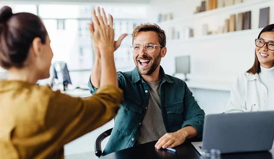 Drei Personen in einem Büro, zwei klatschen sich ab