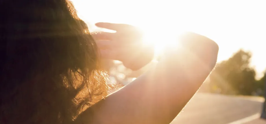 Frau wird von der Sonne geblendet und hält sich die Hand vor die Augen.